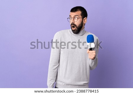 Adult reporter man with beard holding a microphone over isolated purple background doing surprise gesture while looking to the side Royalty-Free Stock Photo #2388778415