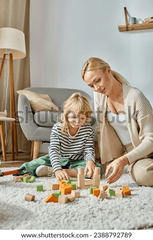 little girl with prosthetic leg sitting on carpet and playing with wooden toys near blonde mother Royalty-Free Stock Photo #2388792789