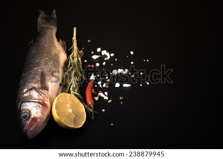 Fresh sea fish lying on dark background with spices. Space for text