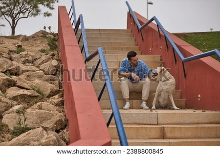 Young Hispanic man, sitting on stairs next to his dog while talking with him in a loving and tender attitude. Concept, dogs, pets, animals, friends. Royalty-Free Stock Photo #2388800845