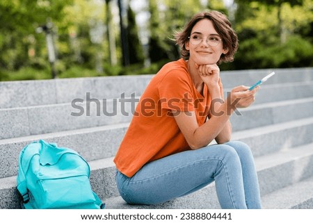 Photo of cute thoughtful girl dressed orange t-shirt eyewear sitting stair texting modern device outdoors urban town park