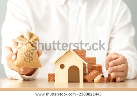 Businessman hand holding the money bag and home model and brick put on the desk in the office, Loan for real estate or construction industry a new house and renovation to estate in the future concept.