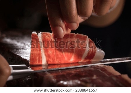 Spanish acorn-fed Iberian ham. Iberian ham cutter hand cutting slice for tasting. Typical high quality slice of Iberian ham with its veins and fat. Royalty-Free Stock Photo #2388841557