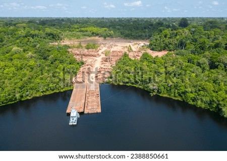 Aerial drone view of a riverbank barge being laden with timber woods harvested from the heart of the Amazon rainforest