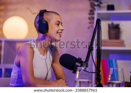 Portrait of a podcaster sitting in a small podcasting studio, wearing headphones and speaking at the microphone while making a podcast episode. A gen z girl is going live on stream during a podcast.