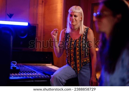 Picture of studio musician snapping fingers to the rhythm of newly recorded music track in a music recording studio. Mixing console and speaker, neon light in the background. 