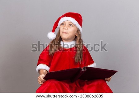 Adorable little girl in Christmas outfit reading Christmas stories in book