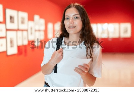 Portrait of a positive girl visitor with an information booklet attending an exhibition of paintings in an art gallery Royalty-Free Stock Photo #2388872315