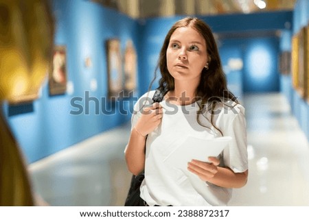 Portrait of an interested visitor girl with an information booklet, viewing an exhibit standing in an art gallery Royalty-Free Stock Photo #2388872317