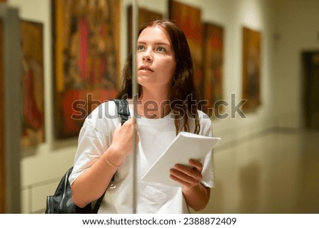 Focused girl visiting an exhibition in a museum looks with interest at the exhibit located behind the glass Royalty-Free Stock Photo #2388872409