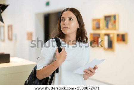 Focused girl visitor with a booklet in her hands examines an exhibit standing in an art gallery Royalty-Free Stock Photo #2388872471