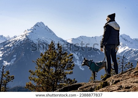woman with dog on summit with snow capped mountains
