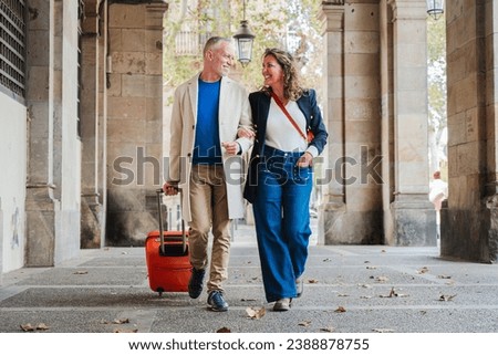 Portrait of a happy mature couple sightseeing on a romantic journey trip in Spain. Middle aged married people walking with a suitcase. Wife and husband smiling and having fun on a weekend tour. High Royalty-Free Stock Photo #2388878755