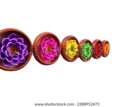 In the picture, there are six brown clay pots with colored lotus-shaped candles placed in them. Purple, pink, yellow, green, red, and orange lotus-shaped candles are arranged in a row.