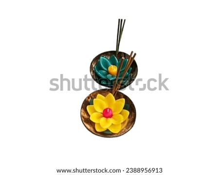 Pictured is a yellow and green lotus candle and three incense sticks in the center of the candle in a brown coconut shell.