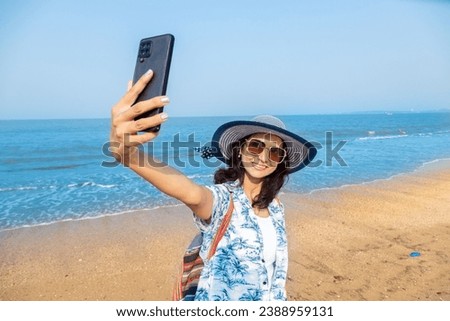 Young Indian woman in summer casual clothes taking a selfie picture with smart phone at beach. Travel, vacations concept. Holidays in lakshadweep. Copy space. Solo traveler. Enjoying life. 
