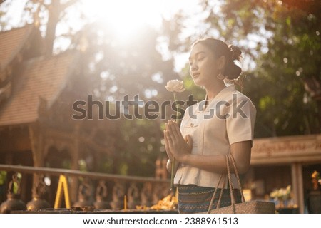 Side view image of a beautiful Asian woman in a traditional Thai-Lanna dress with a lotus flower in her hands is making a wish in a temple. praying, paying respect to the Buddha, Thai culture Royalty-Free Stock Photo #2388961513
