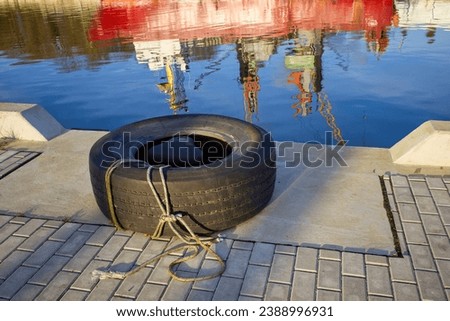 Old tire. Fender on bollard. Reflection in the water of a ship in the port.
