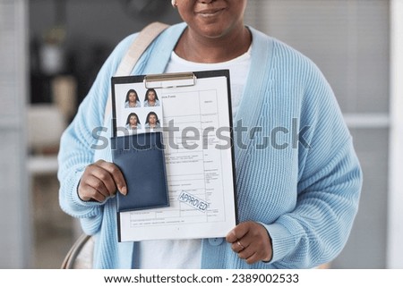 Cropped shot of young African American woman in blue cardigan showing filled visa application form with approve stamp Royalty-Free Stock Photo #2389002533