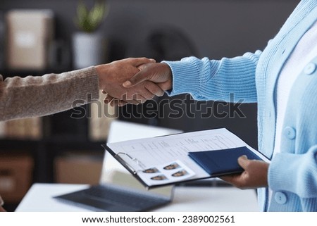 Focus on handshake of female manager of visa application center and young applicant with filled form, passport and photos Royalty-Free Stock Photo #2389002561