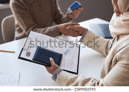 Close-up of approved visa application form and passport in hand of young female applicant against her handshake with manager holding stamp Royalty-Free Stock Photo #2389002595