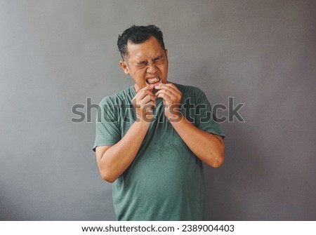 Portrait of asian man using green shirt on touching his mouth and feeling a little pain like ulcerative stomatitis on the gums. Gum inflammation. Royalty-Free Stock Photo #2389004403