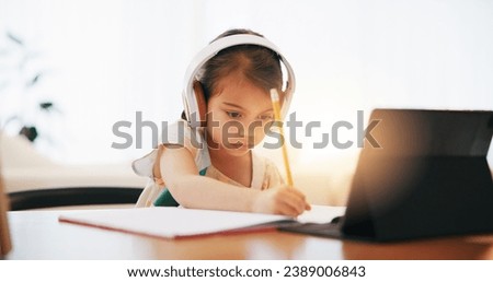 Girl, headphones and writing in book for elearning, education or study on desk at home. Female person, child or kid taking notes with tablet, headset or technology for virtual class at house