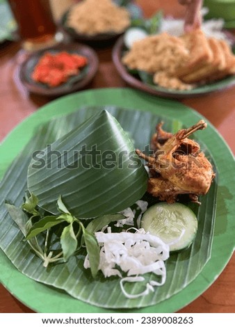 A picture of Indonesian dish named “ayam goreng” made from fried chicken served with vegetable and rice inside a banana leaf cup