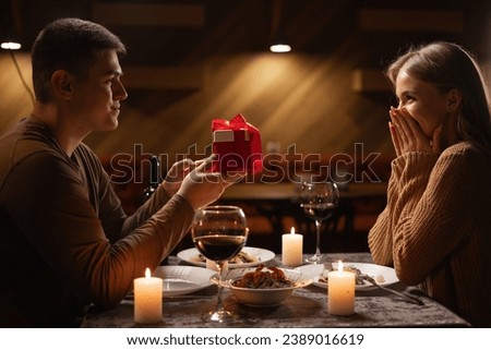 Real candlelight dinner for two, valentine's day date, couple having dinner man giving a woman a gift, romantic family relationship, valentine's day celebration concept Royalty-Free Stock Photo #2389016619