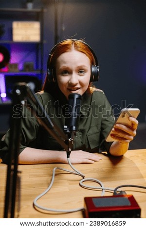 The girl in headphones speaks into the microphone while holding the phone in her hands. The concept of online broadcasts.