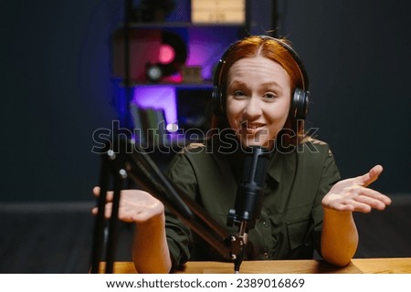 A girl in headphones speaks expressively into a microphone while recording a new blog episode.
