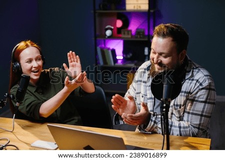 two radio hosts in headphones laughing while recording podcast in studio together
