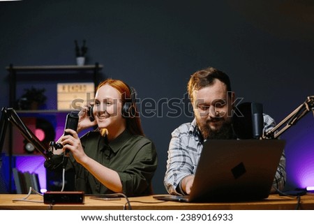 Couple of bloggers in headphones broadcasting live video, broadcasting on air, using sound studio equipment, speaking into microphone, recording video interview.