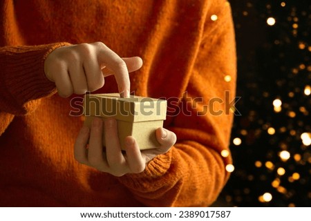 Hands holding a gift box made of kraft paper. child opens a christmas gift against bokeh background