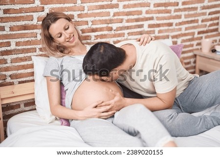 Man and woman couple kissing belly sitting on bed at bedroom