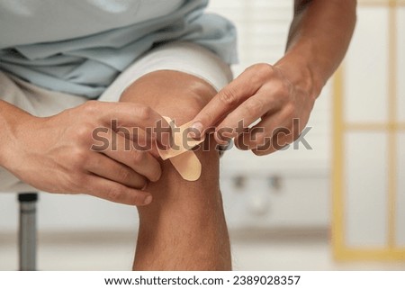 Man putting sticking plasters onto knee indoors, closeup