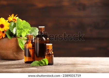 Bottles with essential oils, mint and flowers on wooden table. Space for text