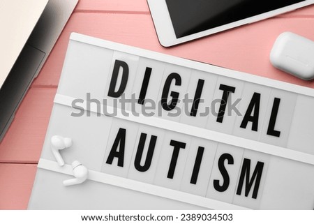 Lightbox with phrase Digital Autism and devices on pink wooden table, flat lay