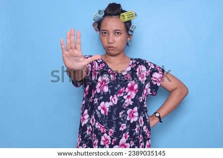 Adult Asian woman with roll hair and casual dress isolated on blue background making stop gesture
