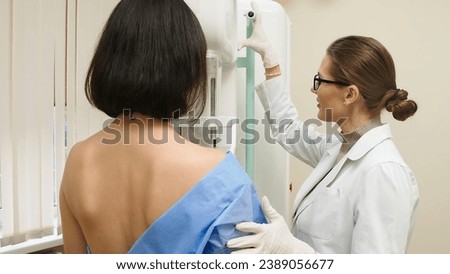 A female doctor in a modern clinic explains the mammography procedure to a topless adult patient undergoing a mammogram. A healthy woman is engaged in cancer prevention in a hospital ward. Royalty-Free Stock Photo #2389056677