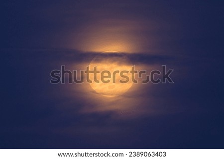 Yellow full moon behind clouds in northern France in summer Royalty-Free Stock Photo #2389063403
