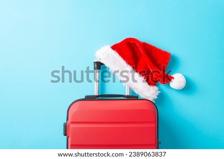 Santa's on the move, making a stop at your party! Top view picture showcasing a red suitcase, Santa's iconic hat, and space for advertising on bright blue surface