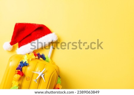 New Year's escape to the islands! Top view composition with suitcase, Santa hat, floral garland, and a mini plane on a cheerful yellow background. Pack your bags for a tropical celebration
