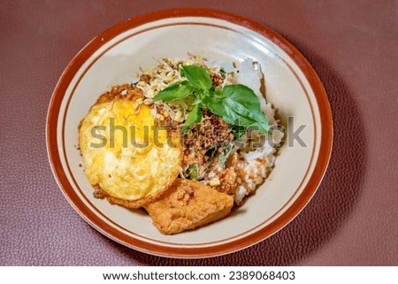 Close picture of Sambel Tumpang with rice, fried egg, some slice cabbage, a toufu, with delicious saouce from tempe and topping with slice of kemangi leaf 
