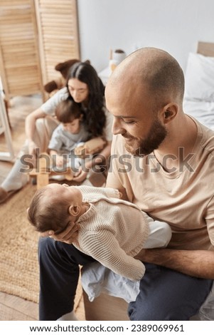focus on father looking lovingly at his newborn baby with blurred wife and little son on backdrop