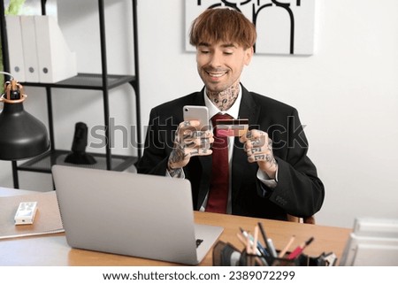 Young businessman with credit card using mobile phone in office