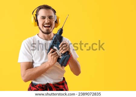 Young man in hearing protectors with drill on yellow background