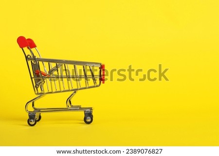 Small metal shopping cart on yellow background. Space for text