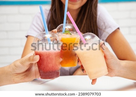 Friends holding drinking together fruity slush drinks.  Royalty-Free Stock Photo #2389079703