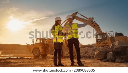 Caucasian Male Engineer Talking To Female Hispanic Architect With Laptop On Construction Site Of Apartment Building. Real Estate Developer Discussing Infrastructure. Heavy Machinery Working. Cinematic Royalty-Free Stock Photo #2389088505